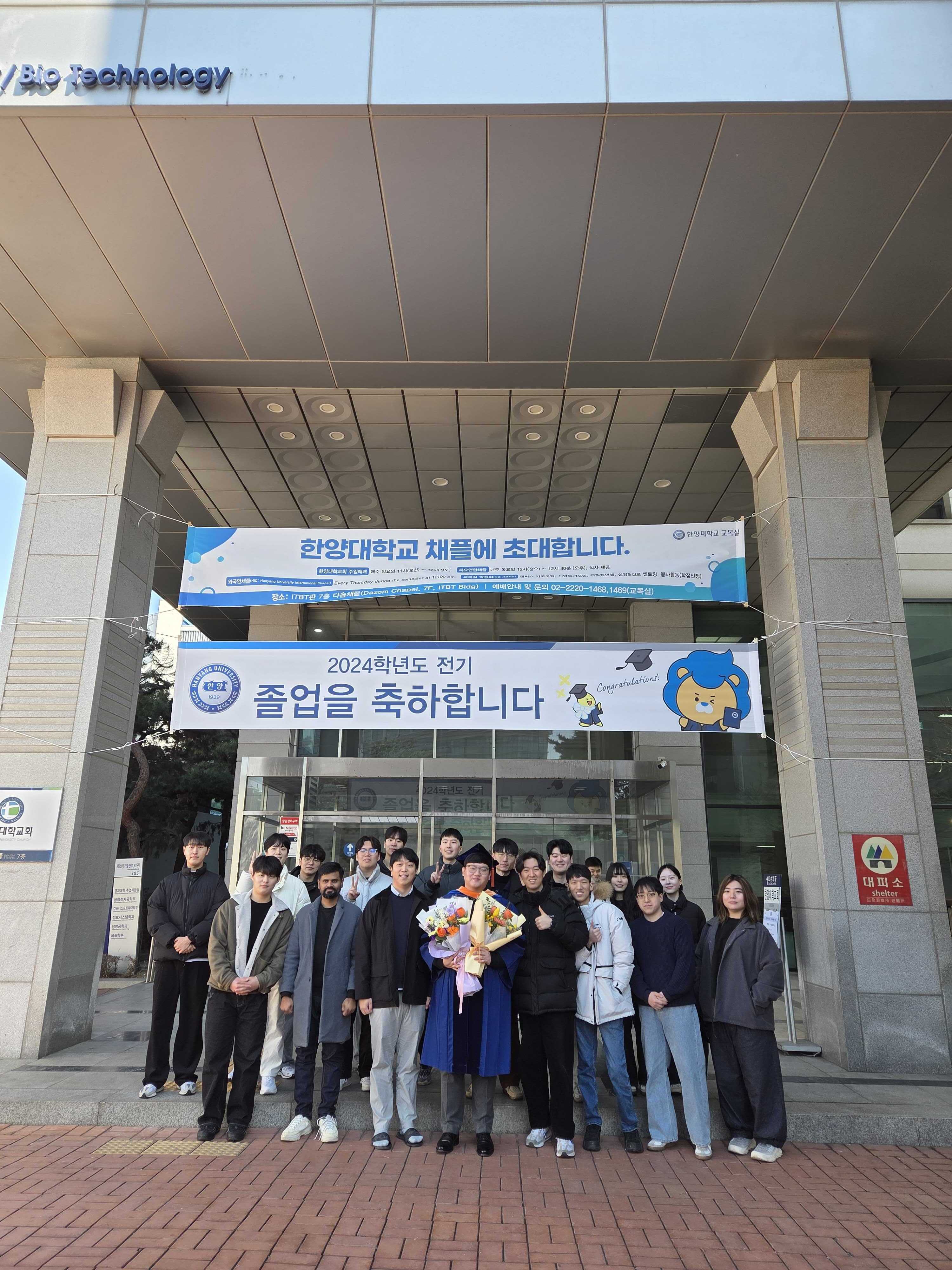 졸업 축하 현수막 앞에서 촬영한 연구실 단체 사진